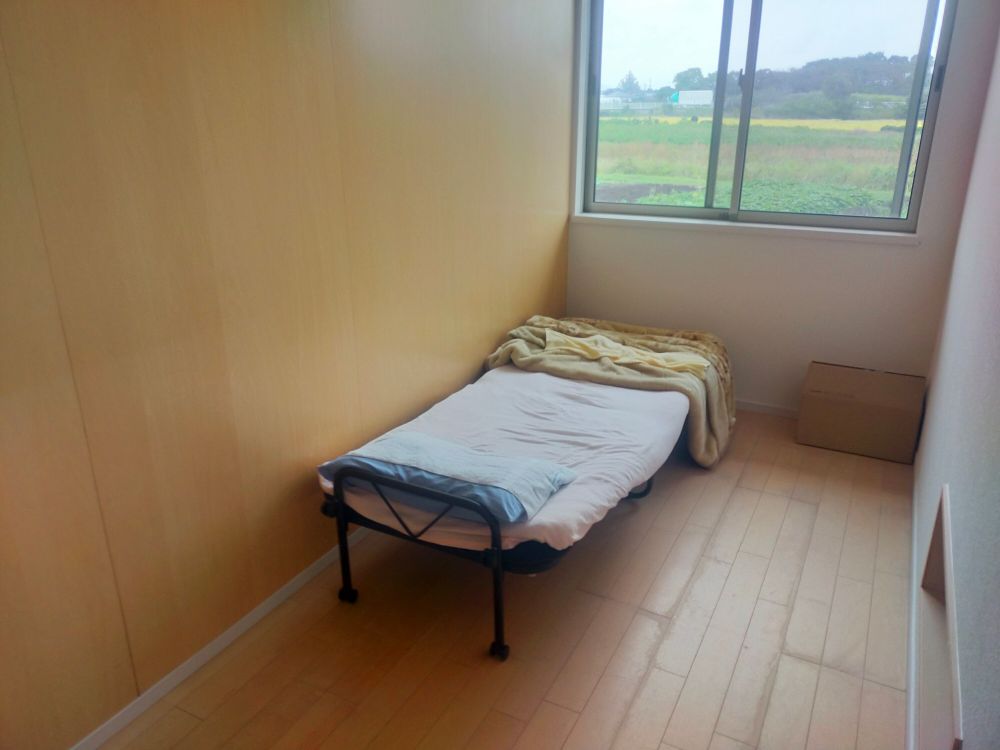 小さな部屋にベッドと布団が用意されている。窓の外には田園が広がっている